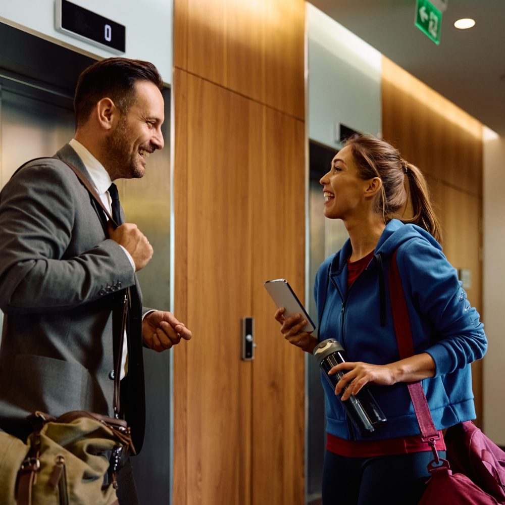 Happy athletic woman talking to a businessman in a hallway at the gym.