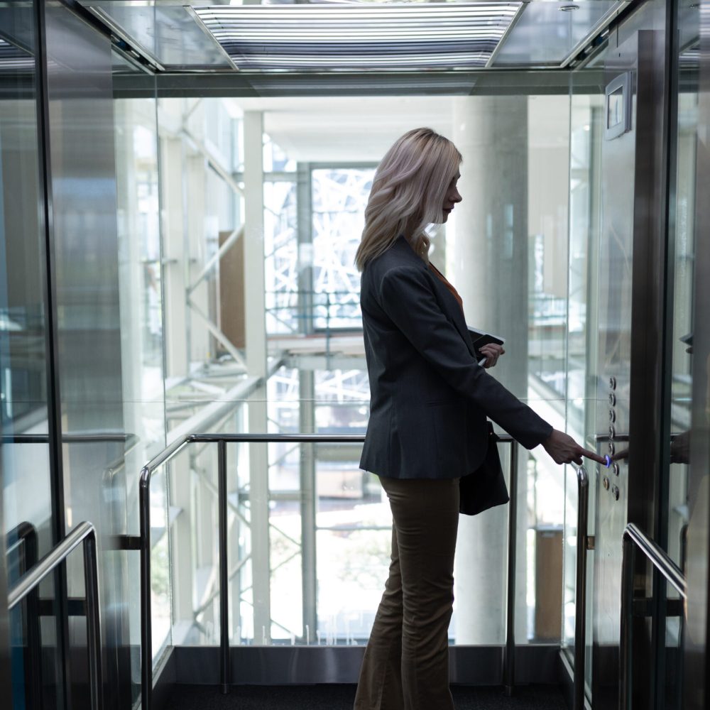Side view of pretty young blonde Caucasian businesswoman using elevator in modern office
